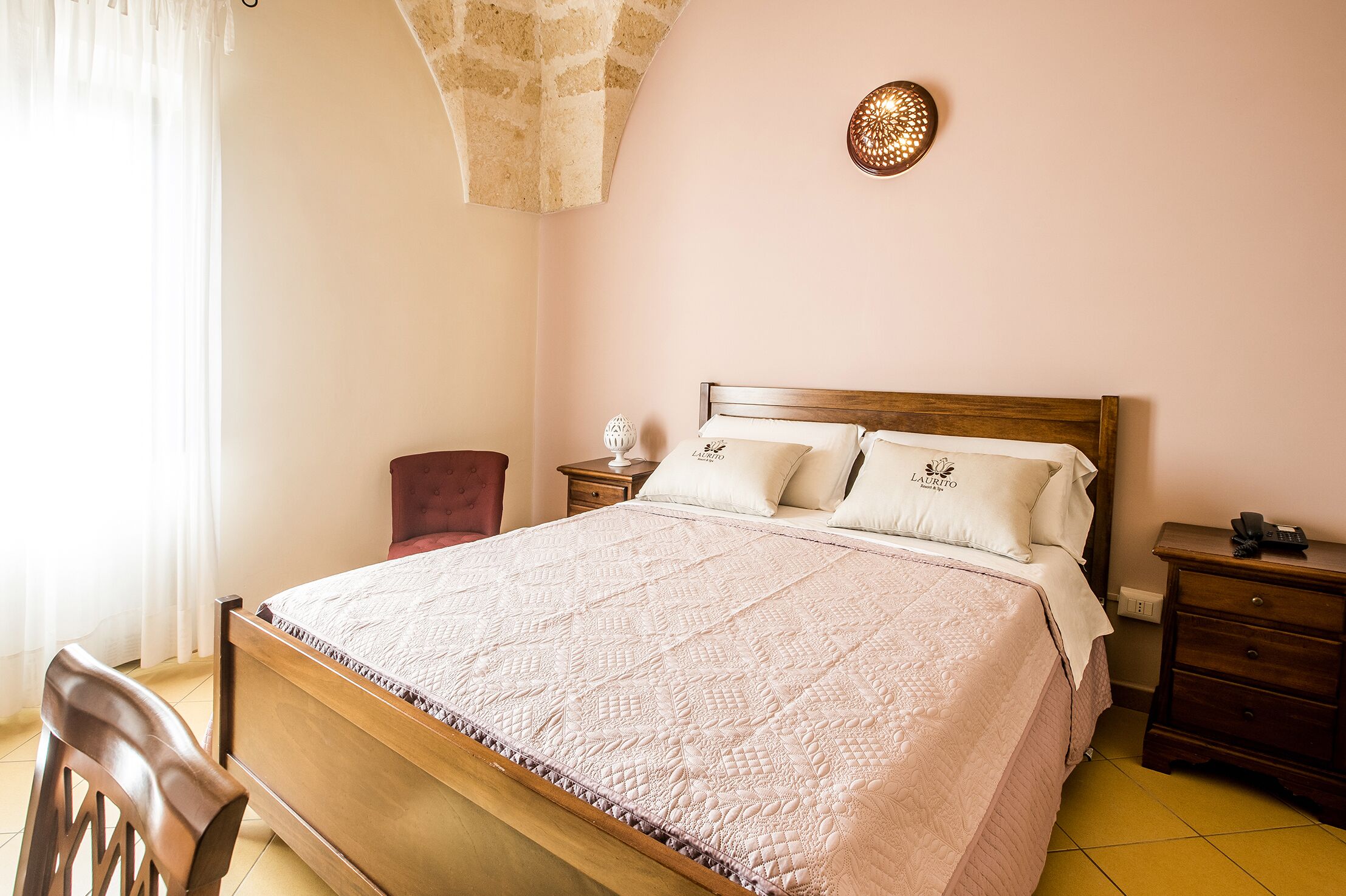 A neatly made bed with a quilted cover, a wooden headboard, and a bedside table with a lamp.