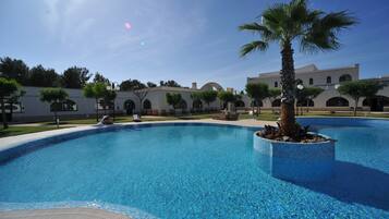 Una piscina con una palmera en una jardinera, rodeada por un edificio con ventanas arqueadas y una terraza con mosaicos.