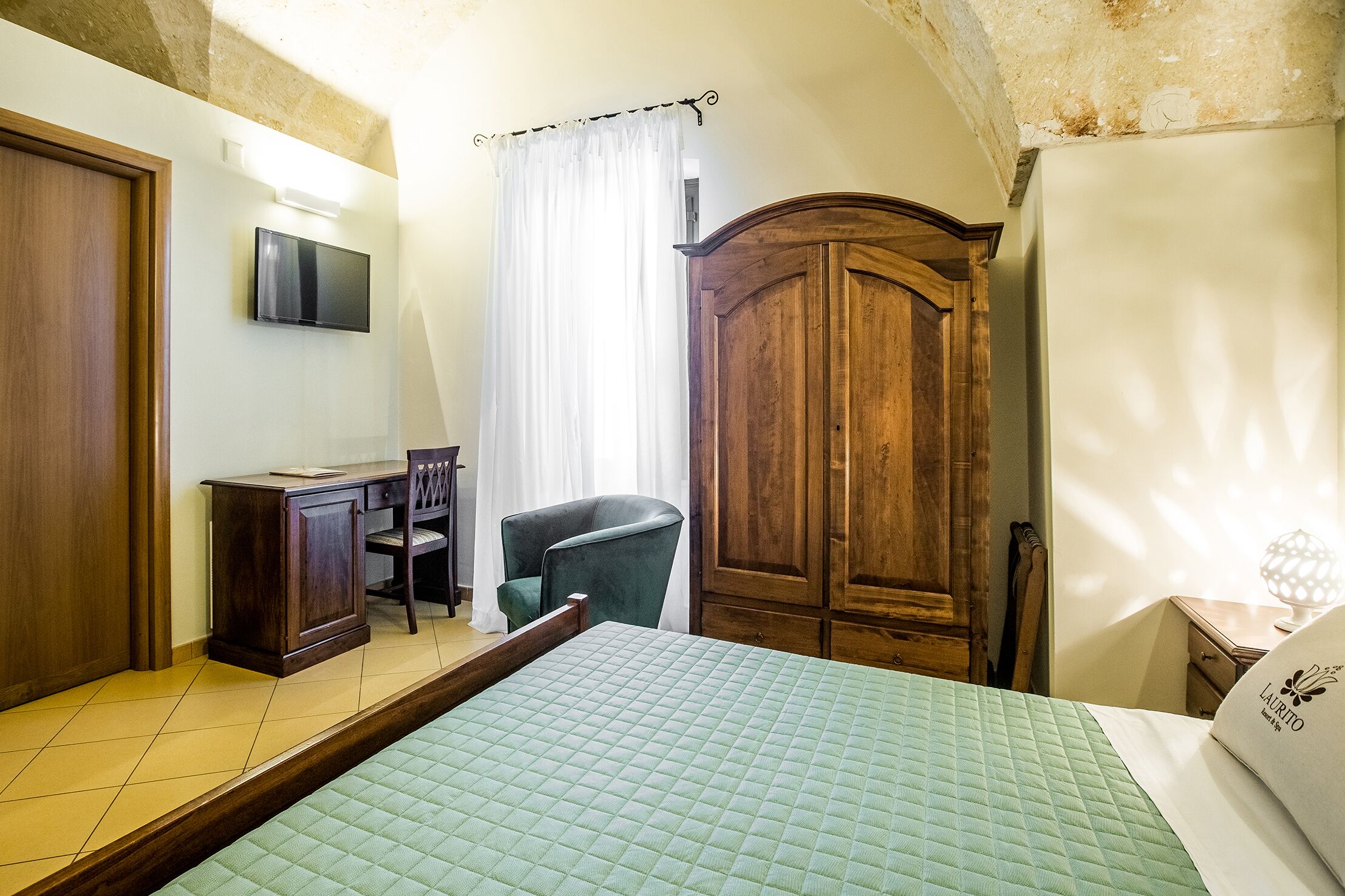 A bedroom with a bed, a desk, a chair, a wardrobe, and a television.