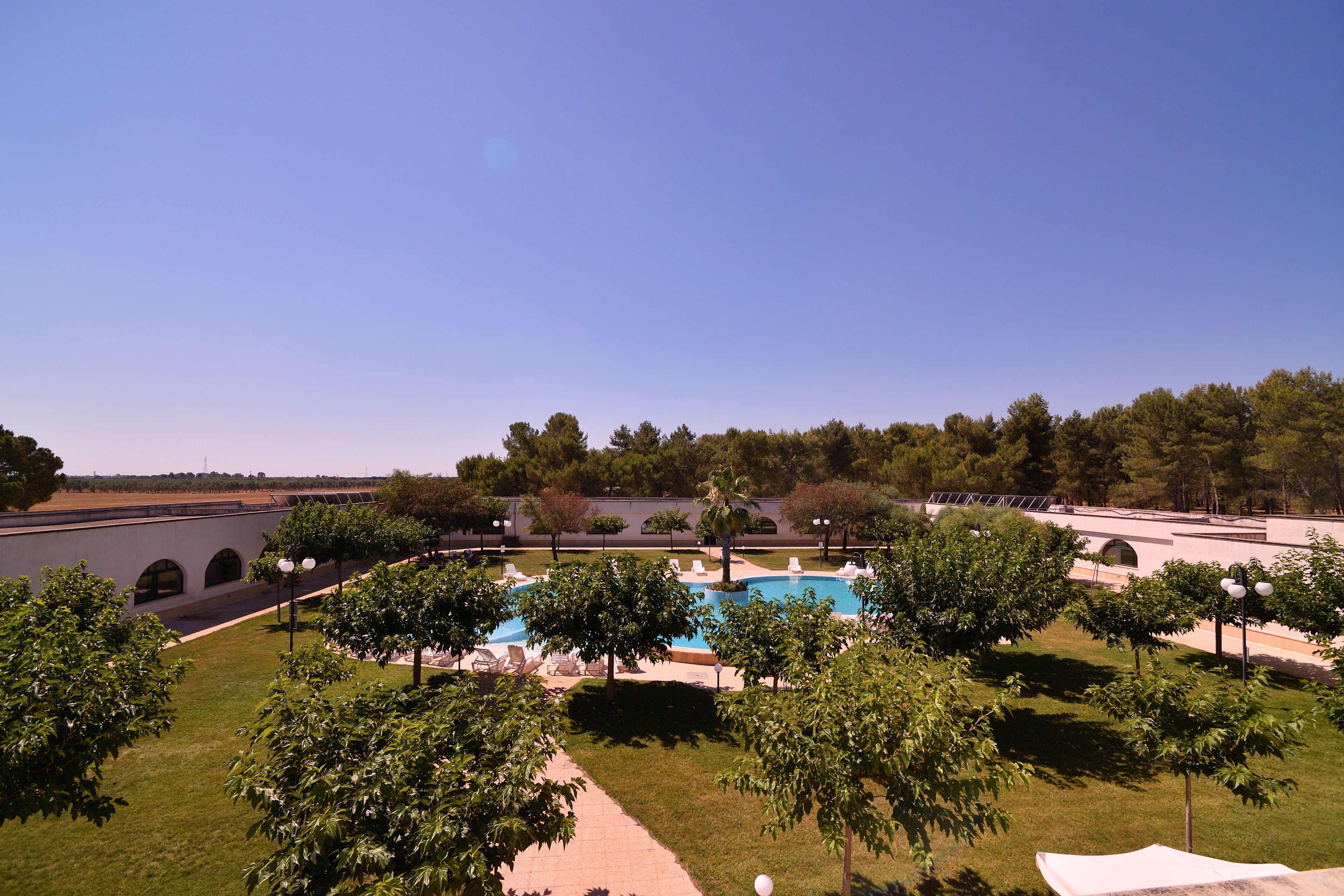 A pool area with lounge chairs and trees, surrounded by a well-maintained lawn and a clear sky.