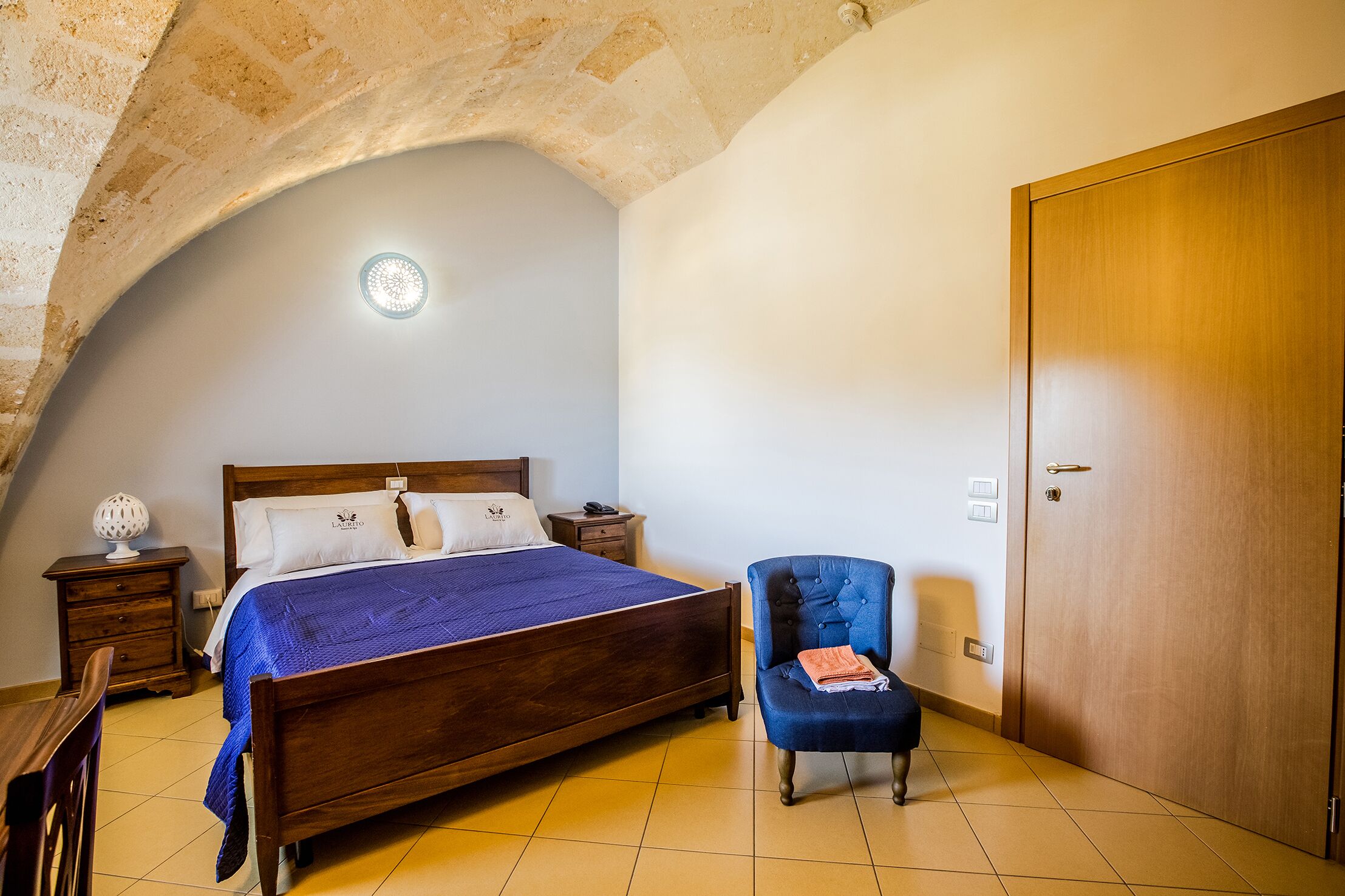 A bedroom with a wooden bed, a nightstand, a chair, and a wooden door.