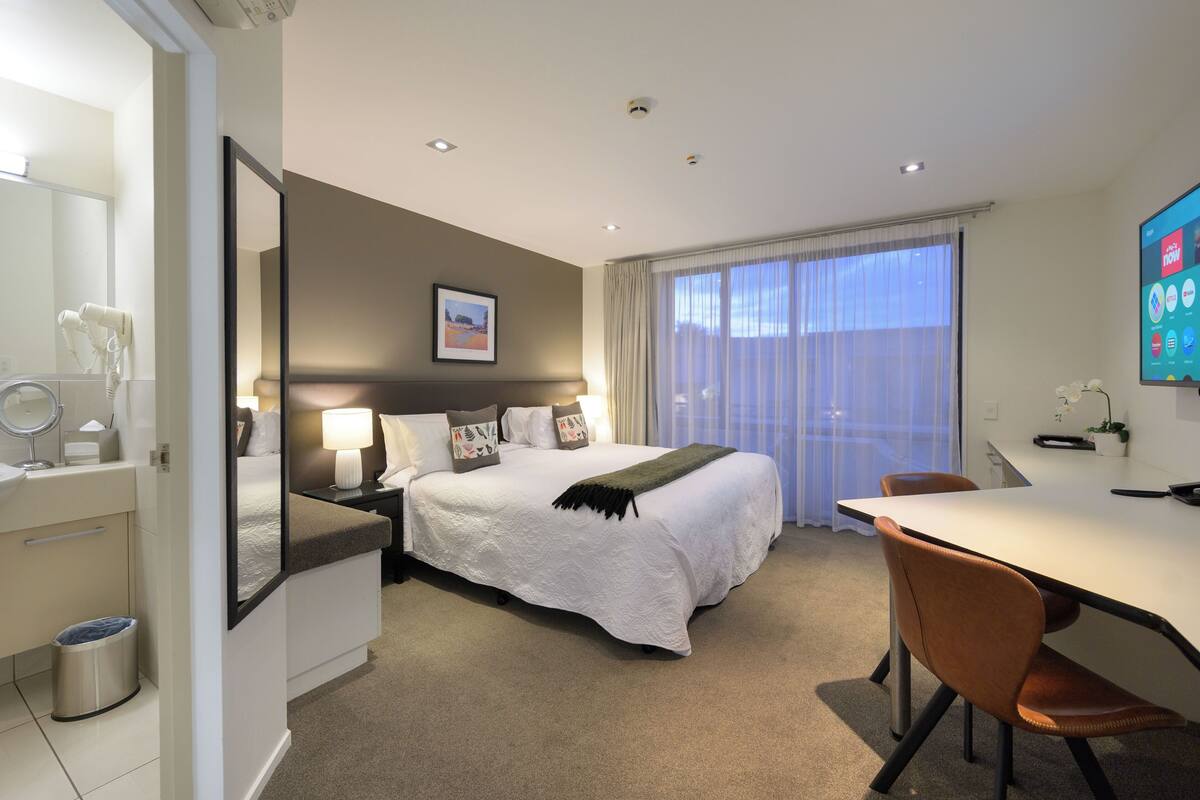 A hotel room with a bed, bedside table, lamp, and a TV on a stand.
