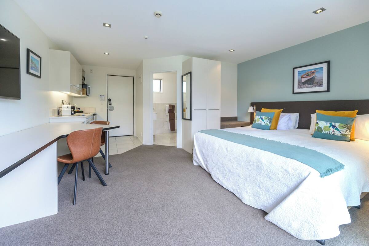 A modern hotel room with a large bed, a desk, and a chair.