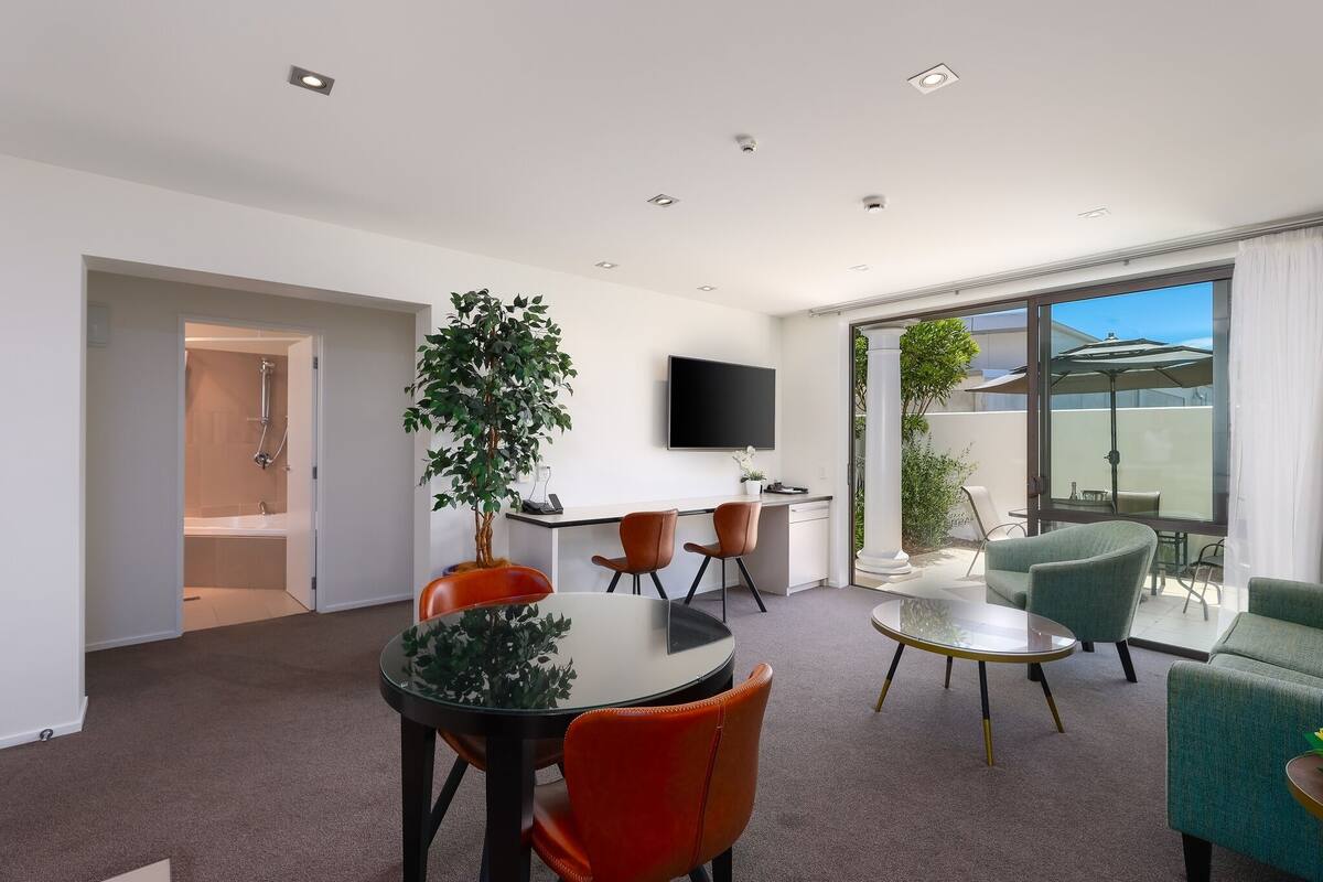 A modern living room with a dining area, a TV mounted on the wall, and a balcony with a view.