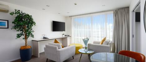 Habitación de hotel moderna con televisión de pantalla plana, una mesa de comedor, un sofá, una silla y una planta en maceta.