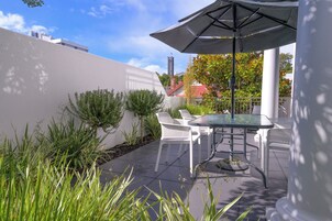 Une terrasse extérieure avec une table et des chaises, entourée de plantes et bordée d’un mur blanc.