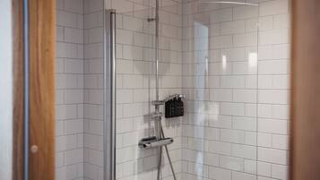 Un espace douche avec des murs recouverts de carreaux blancs, une porte en verre et une pomme de douche à main.