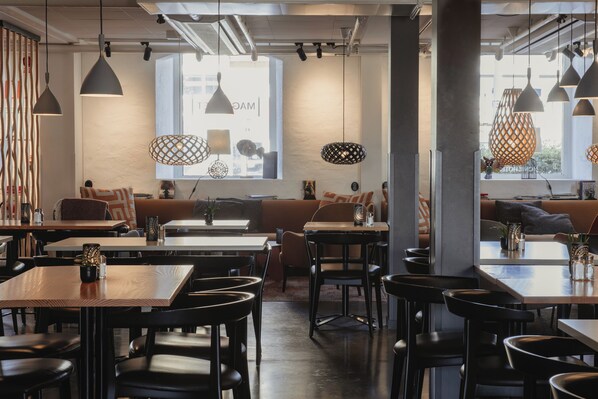 A modern cafe with wooden tables and black chairs, a large window with a view, and pendant lights.
