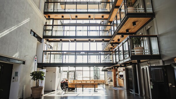 A multi-level interior with a central open space, wooden beams, and glass railings. - Home Hotel Magasinet (Trelleborg)