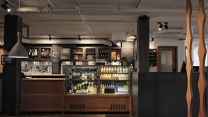A bar area with shelves of bottles, a wooden counter, and a hanging light fixture. - Home Hotel Magasinet (Trelleborg)