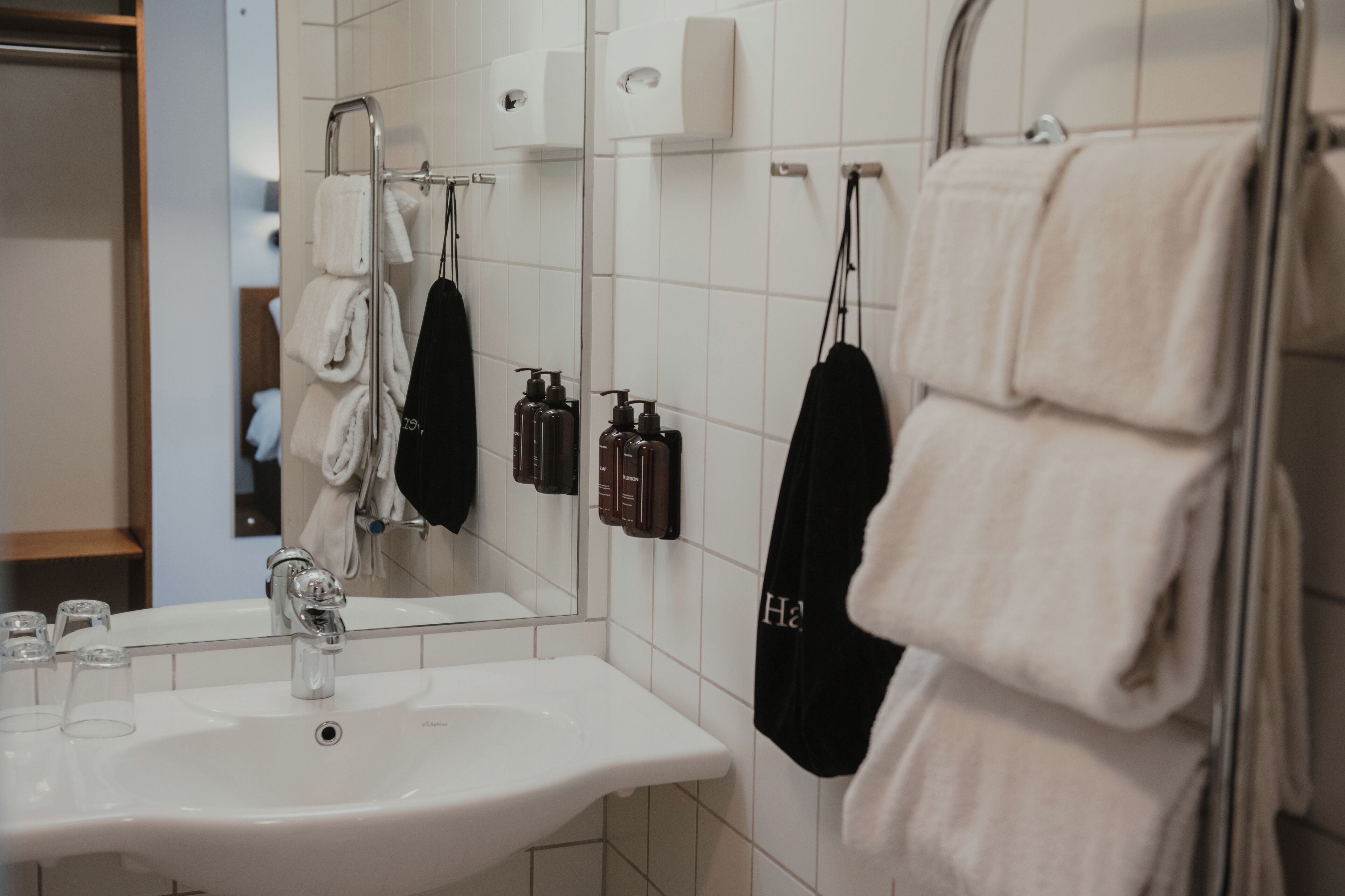 A bathroom with a white sink, mirror, and towel rack with multiple towels.