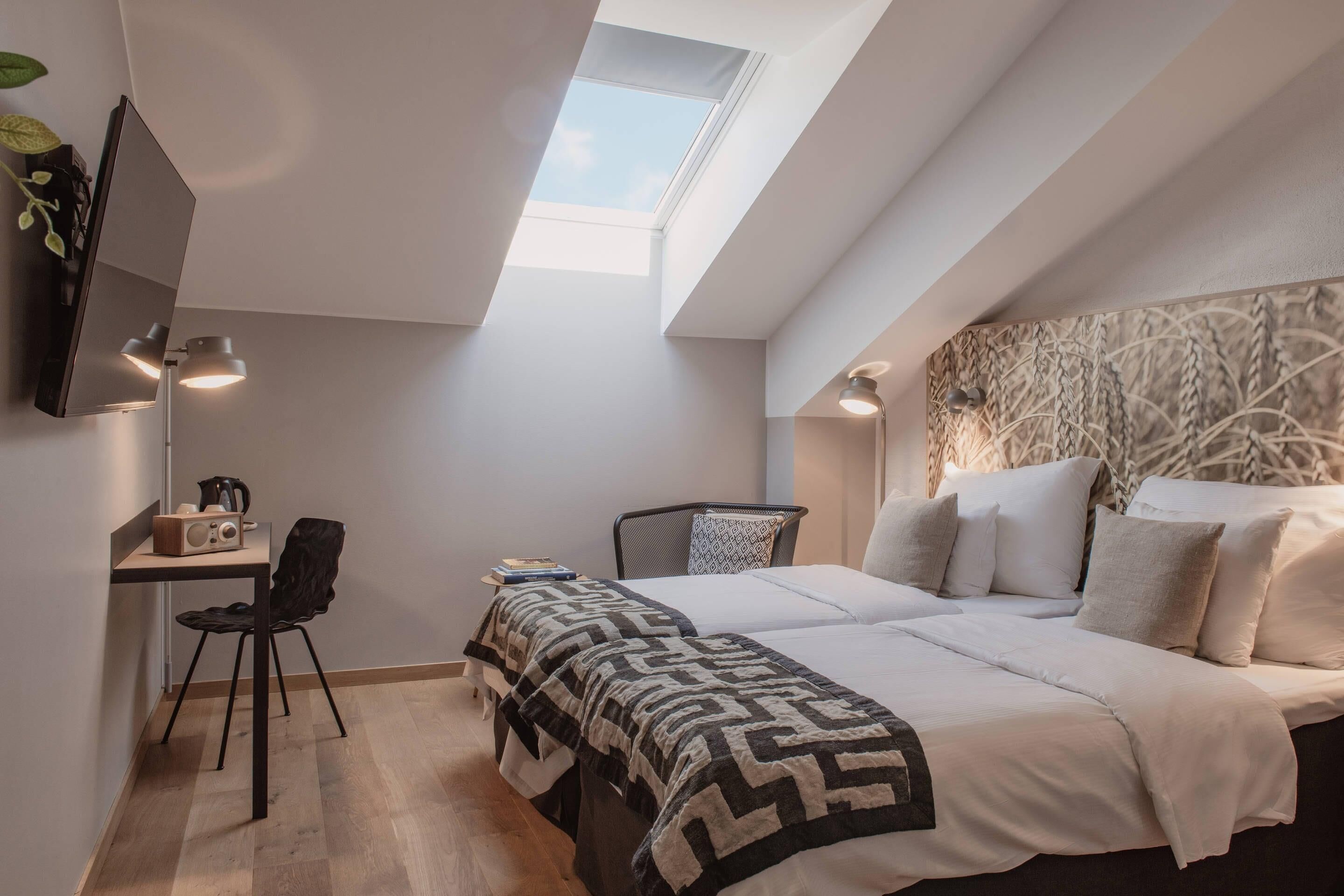 Een moderne slaapkamer met dakraam, een bed met geborduurd sprei, een bureau met stoel en een televisie aan de muur.