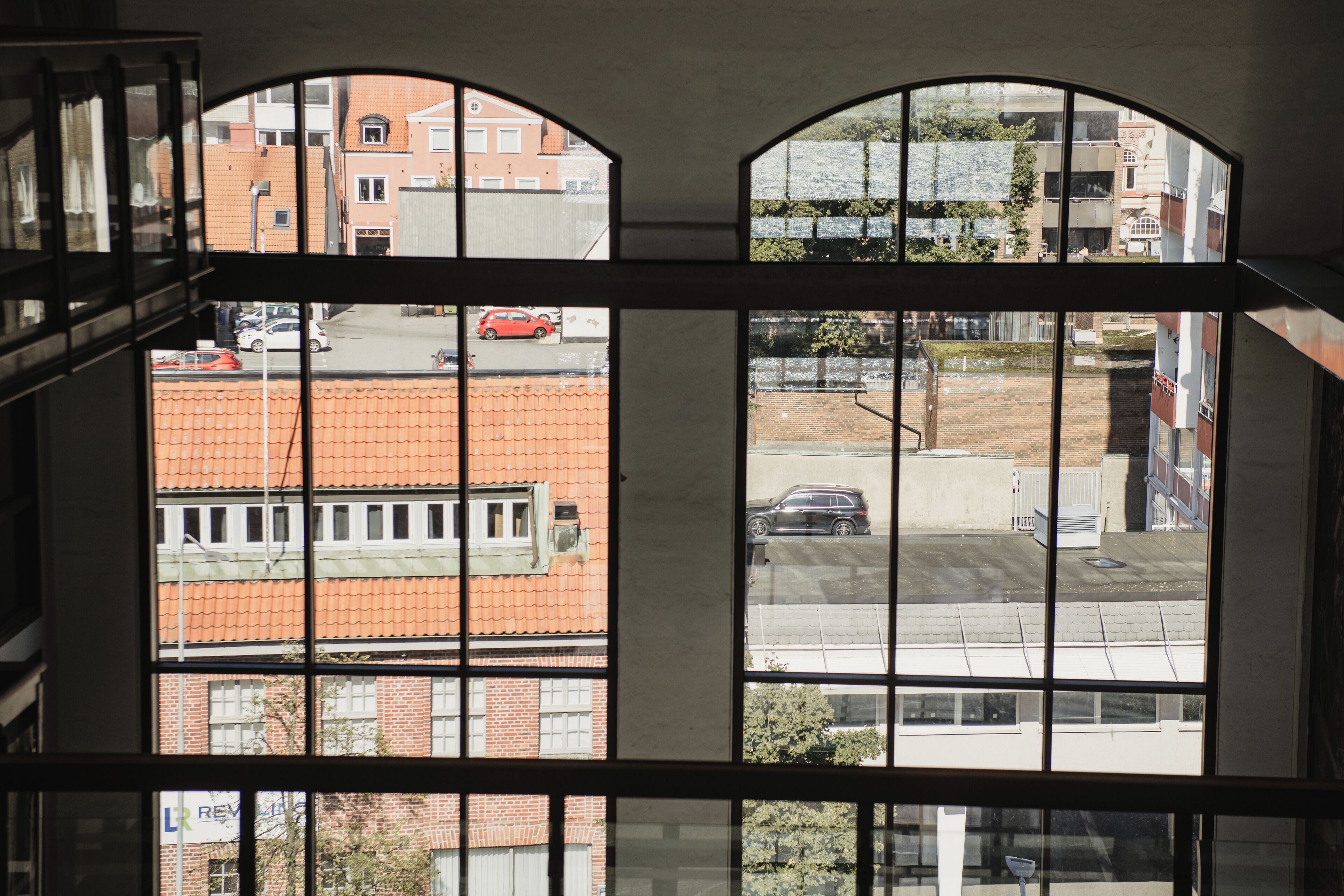 Vista a través de una ventana con un edificio de ladrillo y un coche rojo al frente.