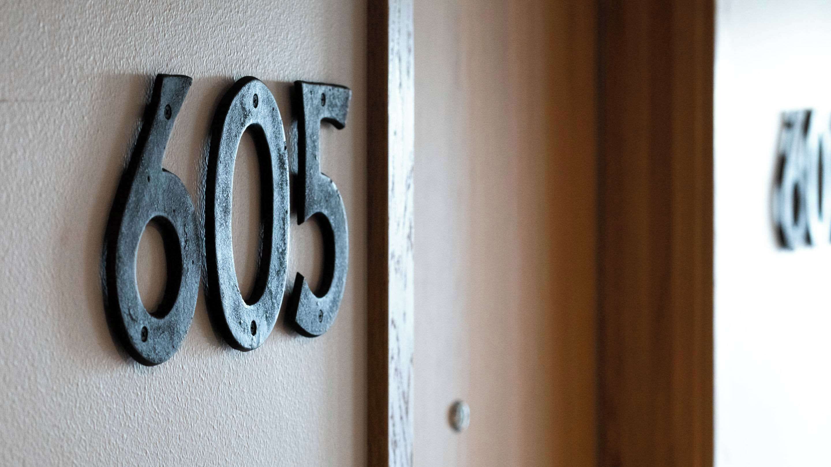 Primer plano de una señal metálica con el número 605 sobre una pared texturizada.
