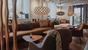 A modern living room with a sofa, armchairs, and a coffee table. There are pendant lights and a large window with a view. - Home Hotel Magasinet (Trelleborg)
