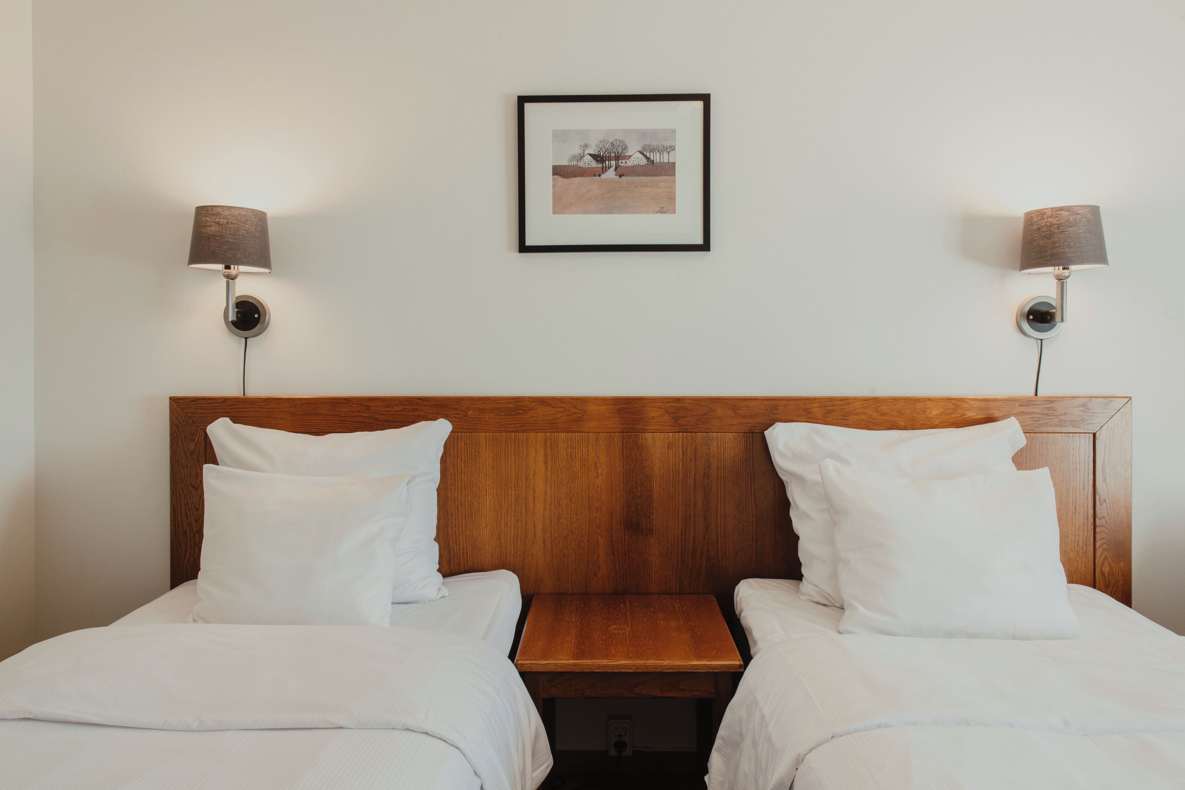 A hotel room with two single beds, a wooden headboard, and two wall-mounted lamps.