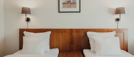 A hotel room with two single beds, a wooden headboard, and two wall-mounted lamps.
