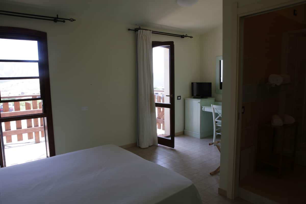 A bedroom with a bed, a TV, and a bathroom visible through an open door.