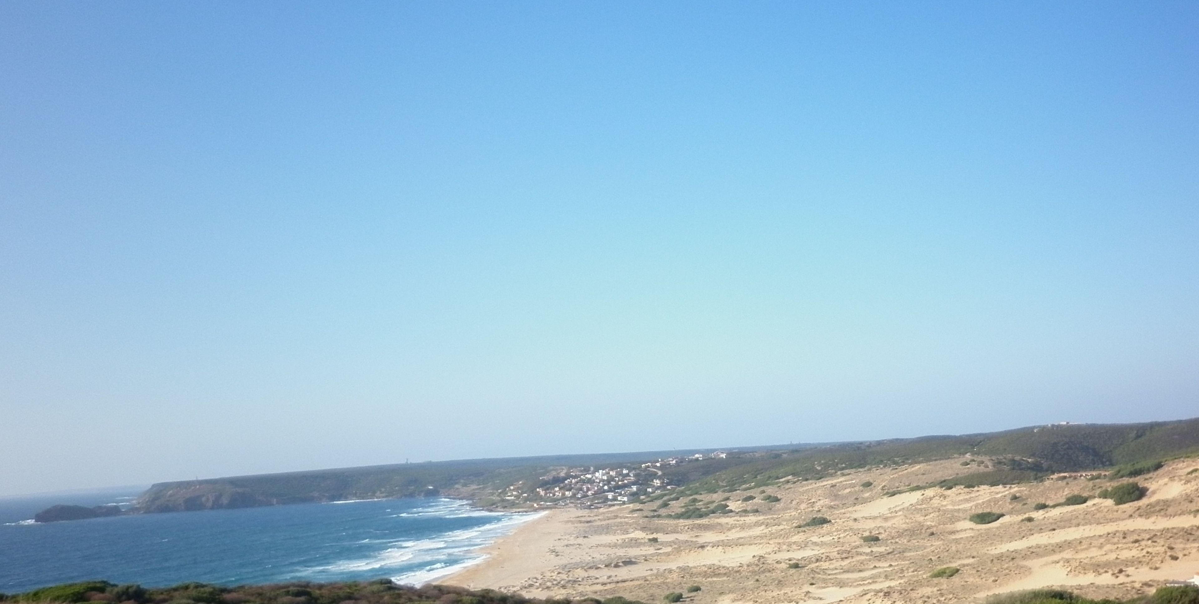 A coastal landscape with a beach, cliffs, and a clear sky.