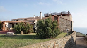 Un edificio de piedra con balcón, rodeado de vegetación y un muro de piedra.