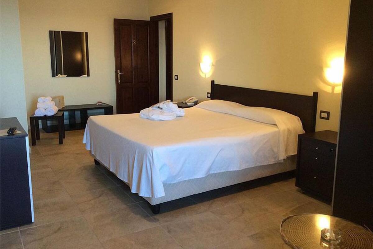 A hotel room with a bed, bedside table, lamp, and a door.