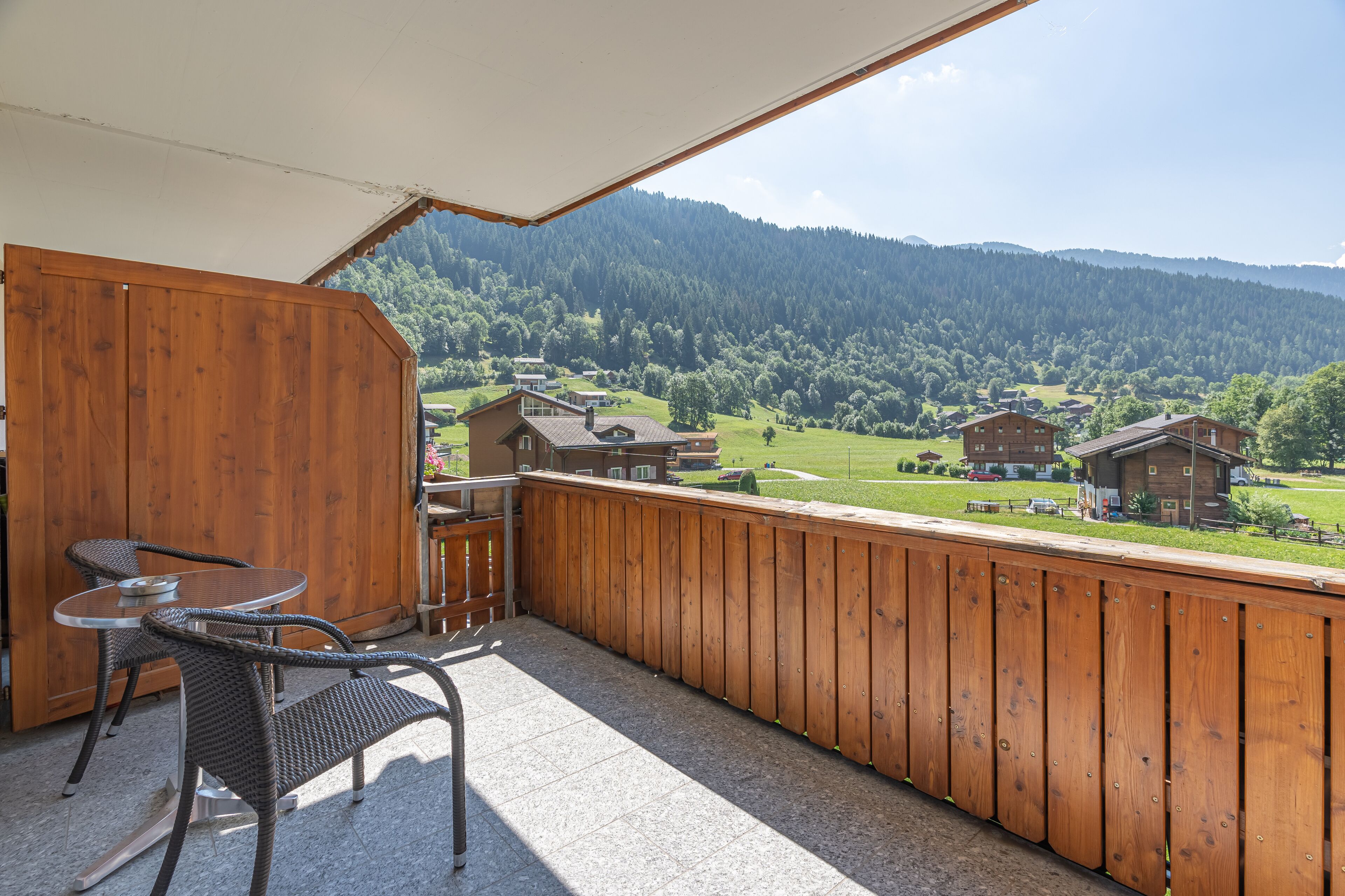 Ein Balkon mit Holzgeländer, Korbstühlen und einem Tisch.