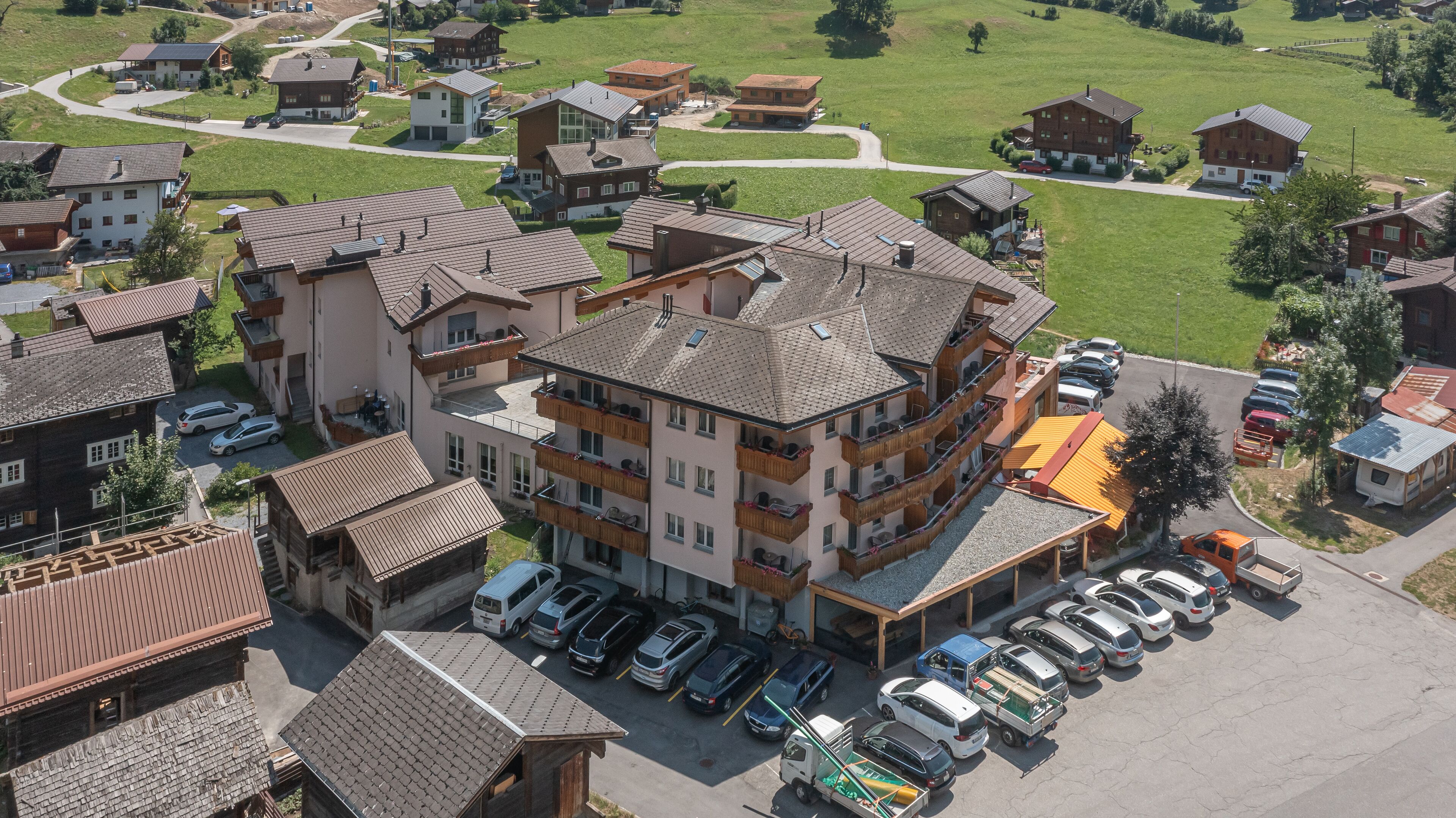 Un hôtel à plusieurs étages doté d’un parking, entouré de champs verdoyants et d’autres bâtiments.