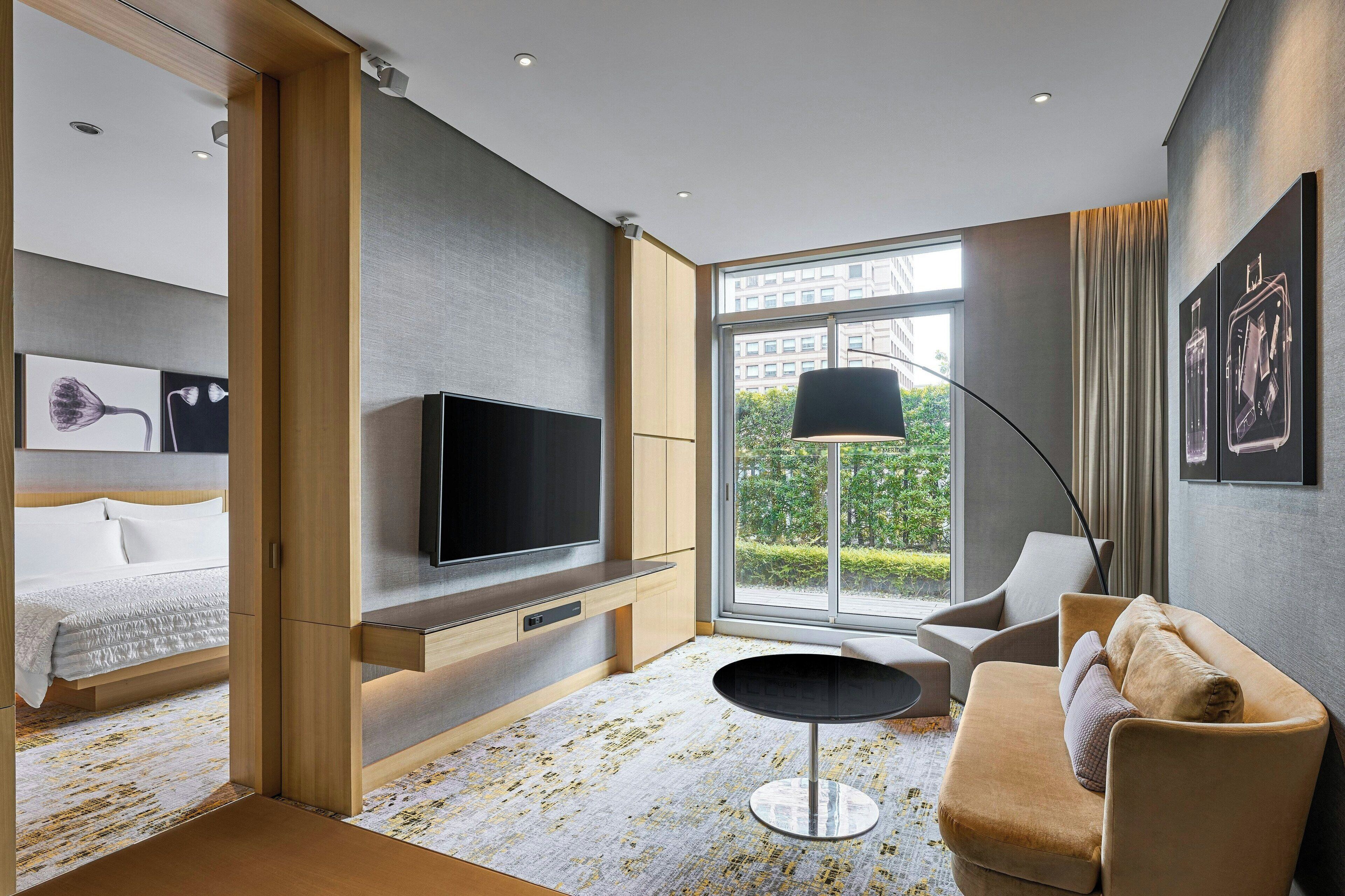 A modern hotel room with a large bed, a TV, a sofa, and a dining table.