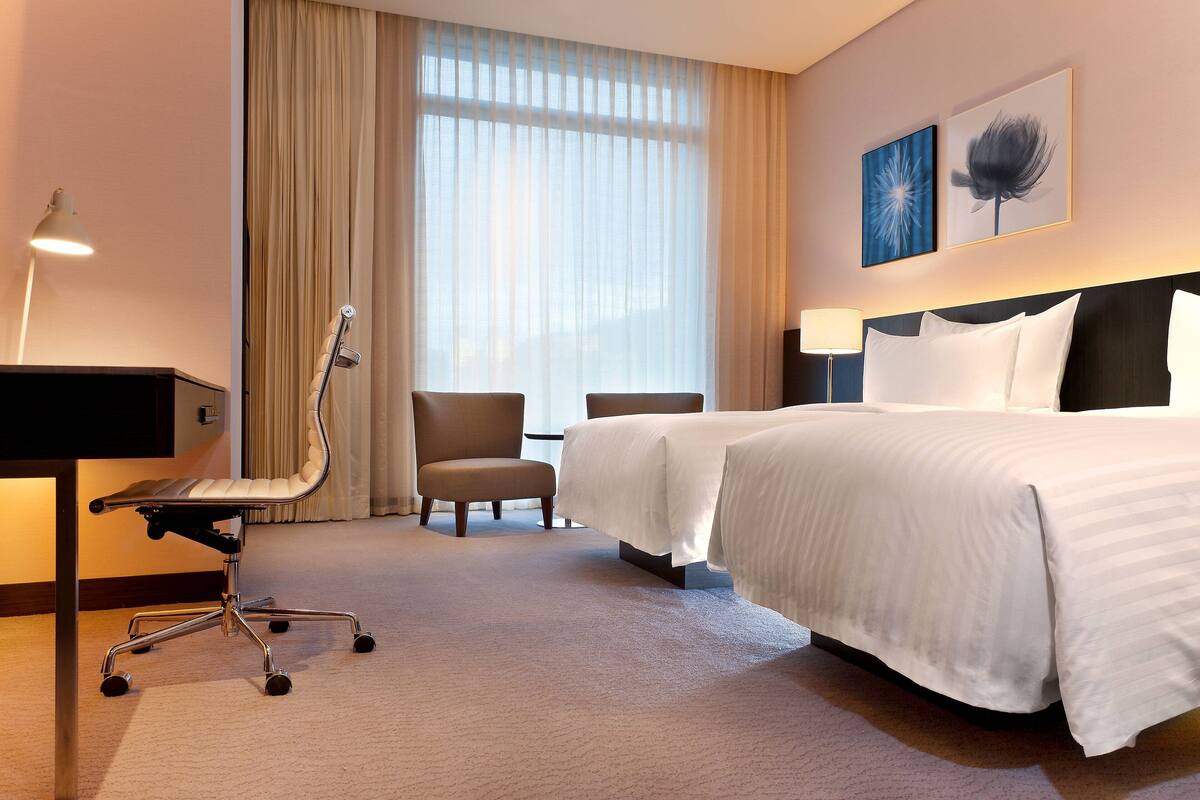 A hotel room with a bed, a desk, a chair, and a large window with curtains.