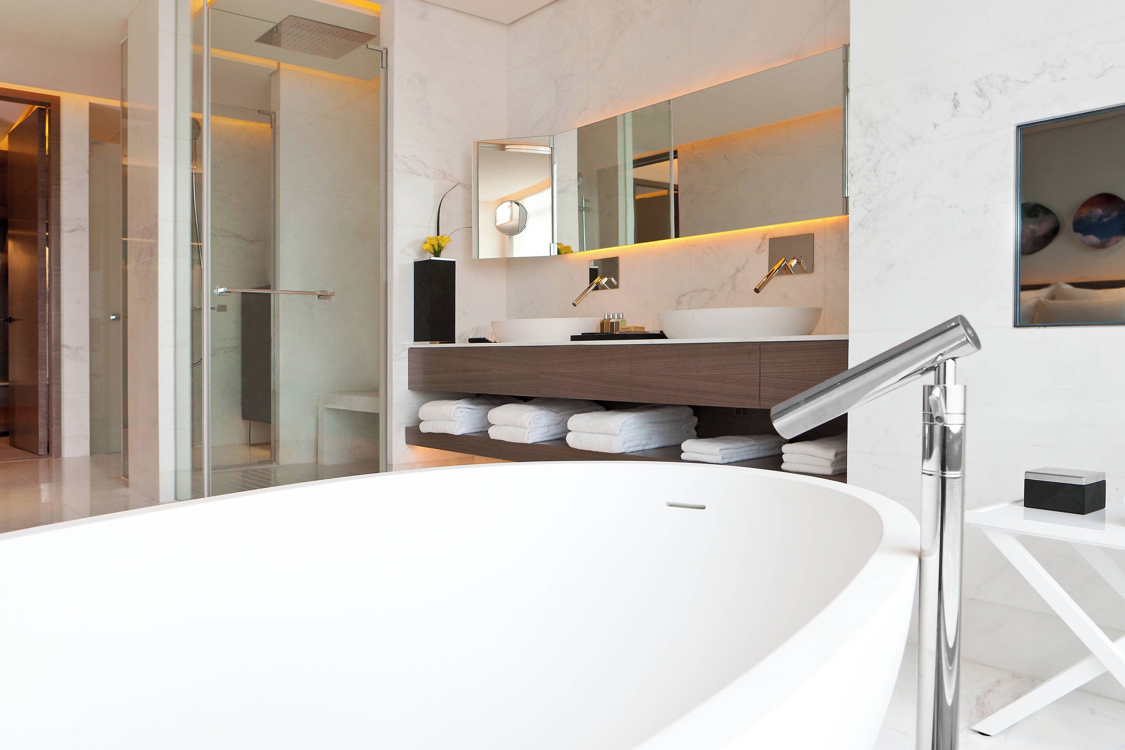 A modern bathroom with a large white bathtub, a glass-enclosed shower, and a wooden vanity with a large mirror.