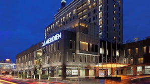 Um hotel moderno com um destaque para a placa 'Le Meridien', apresentando uma estrutura em vários andares com varandas e uma fachada bem iluminada.