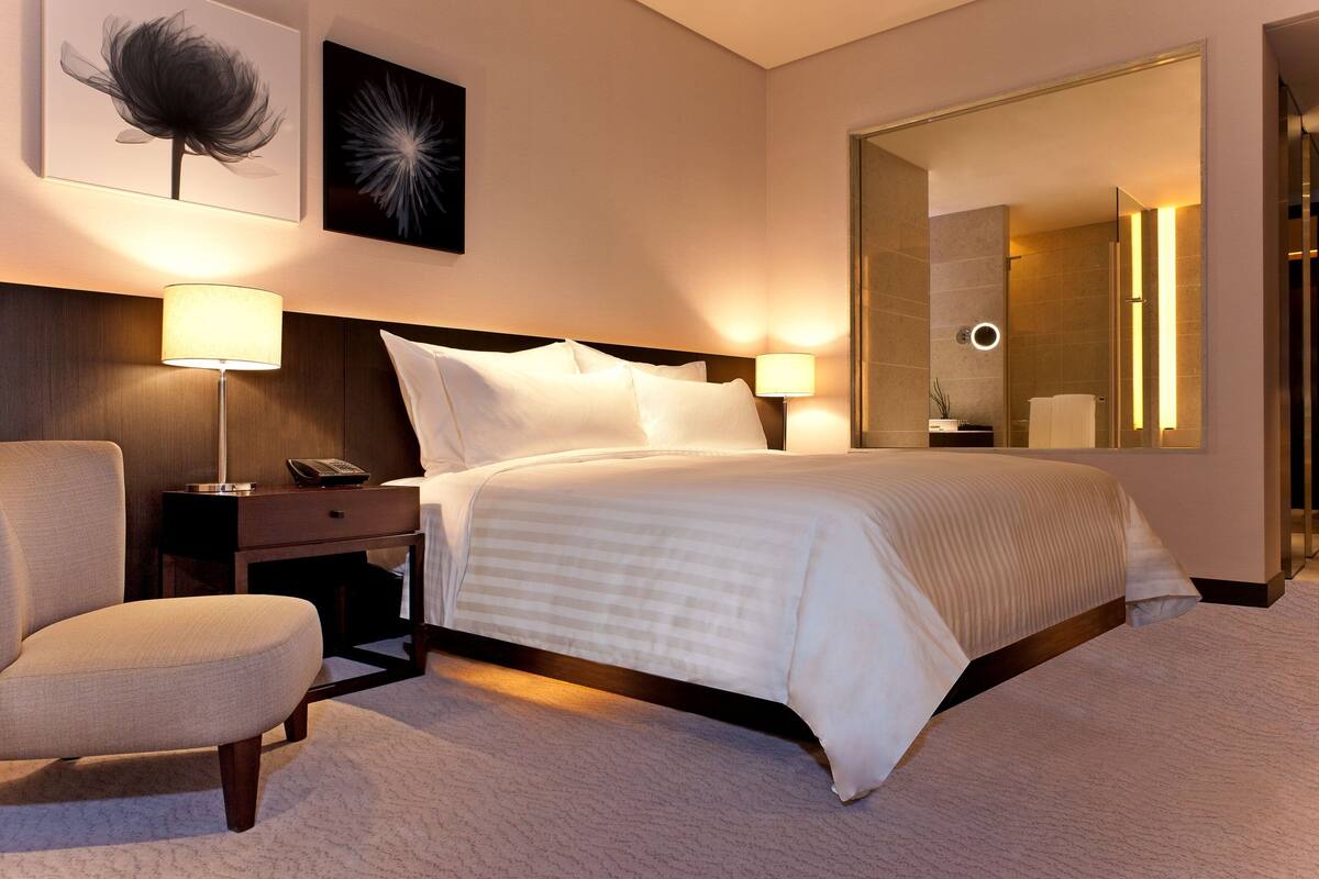 A hotel room with a large bed, two bedside lamps, a nightstand with a phone, a chair, and a large mirror.