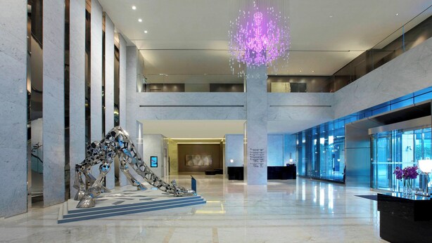 Um lobby amplo com um lustre moderno, uma escultura metálica única e um balcão de recepção.