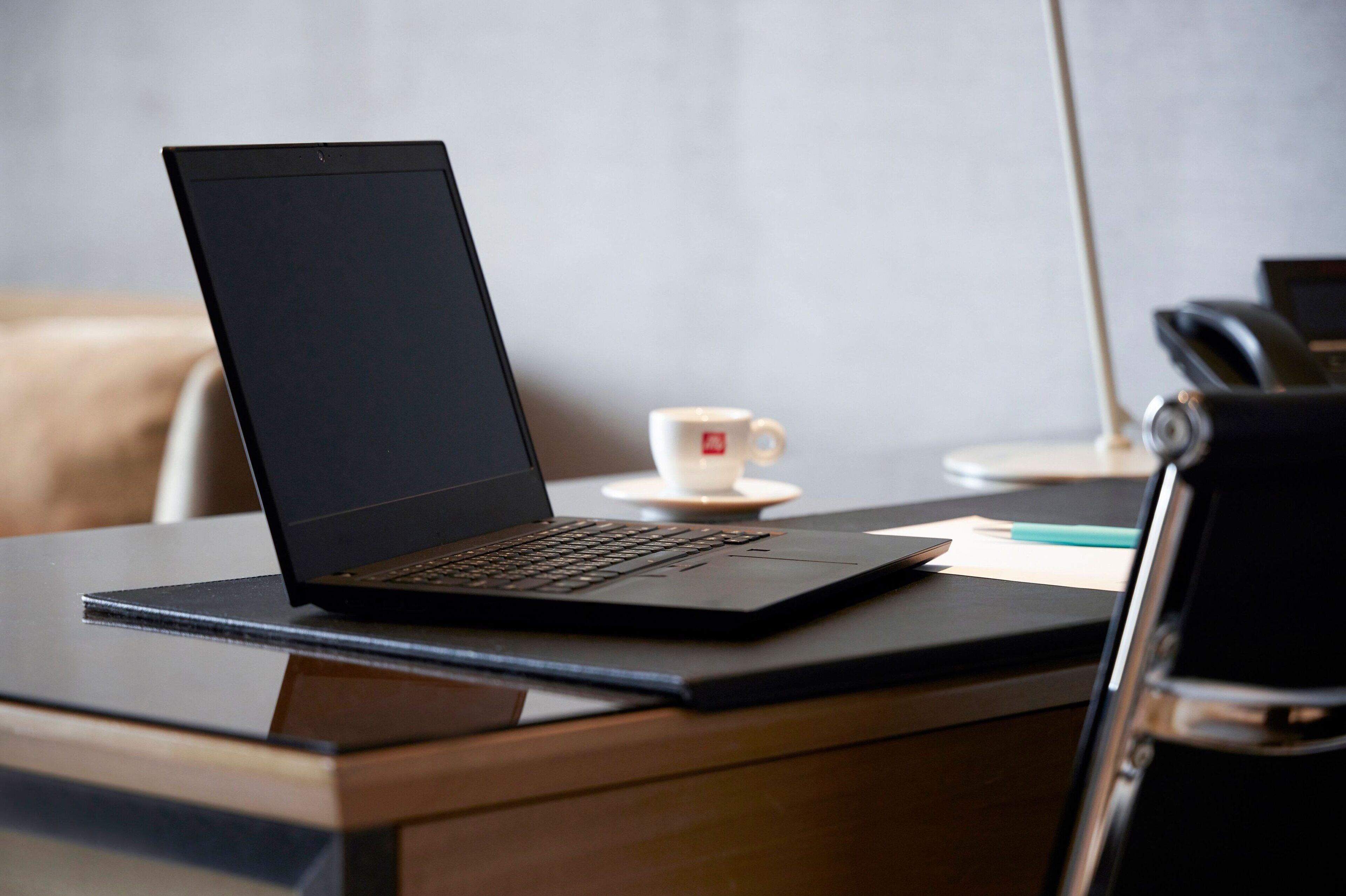 A laptop on a wooden desk with a white cup and a pen.
