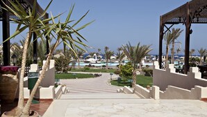 A hotel entrance with a pool view, palm trees, and a clear sky. -  Three Corners Sea Beach Resort (El Quseir)
