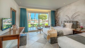 A hotel room with a bed, a desk, and a TV. There is a view of a pool and palm trees outside the window. -  Three Corners Sea Beach Resort (El Quseir)