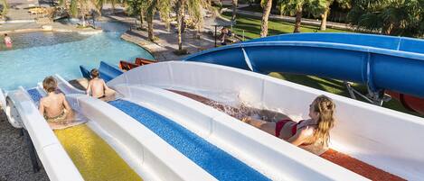Um toboágua em um resort, com várias pistas, palmeiras e uma piscina ao fundo.