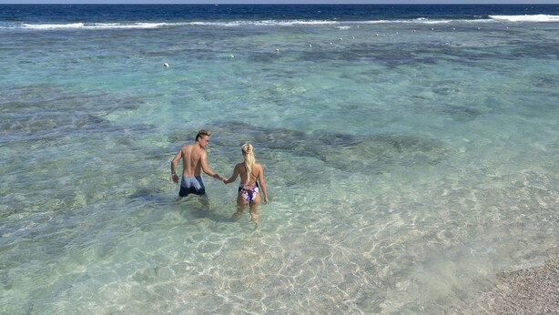 A couple walking hand in hand in shallow clear water, with a beach and ocean in the background. -  Three Corners Sea Beach Resort (El Quseir)