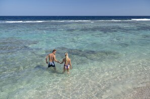 A couple walking hand in hand in shallow clear water, with a beach and ocean in the background. -  Three Corners Sea Beach Resort (El Quseir)