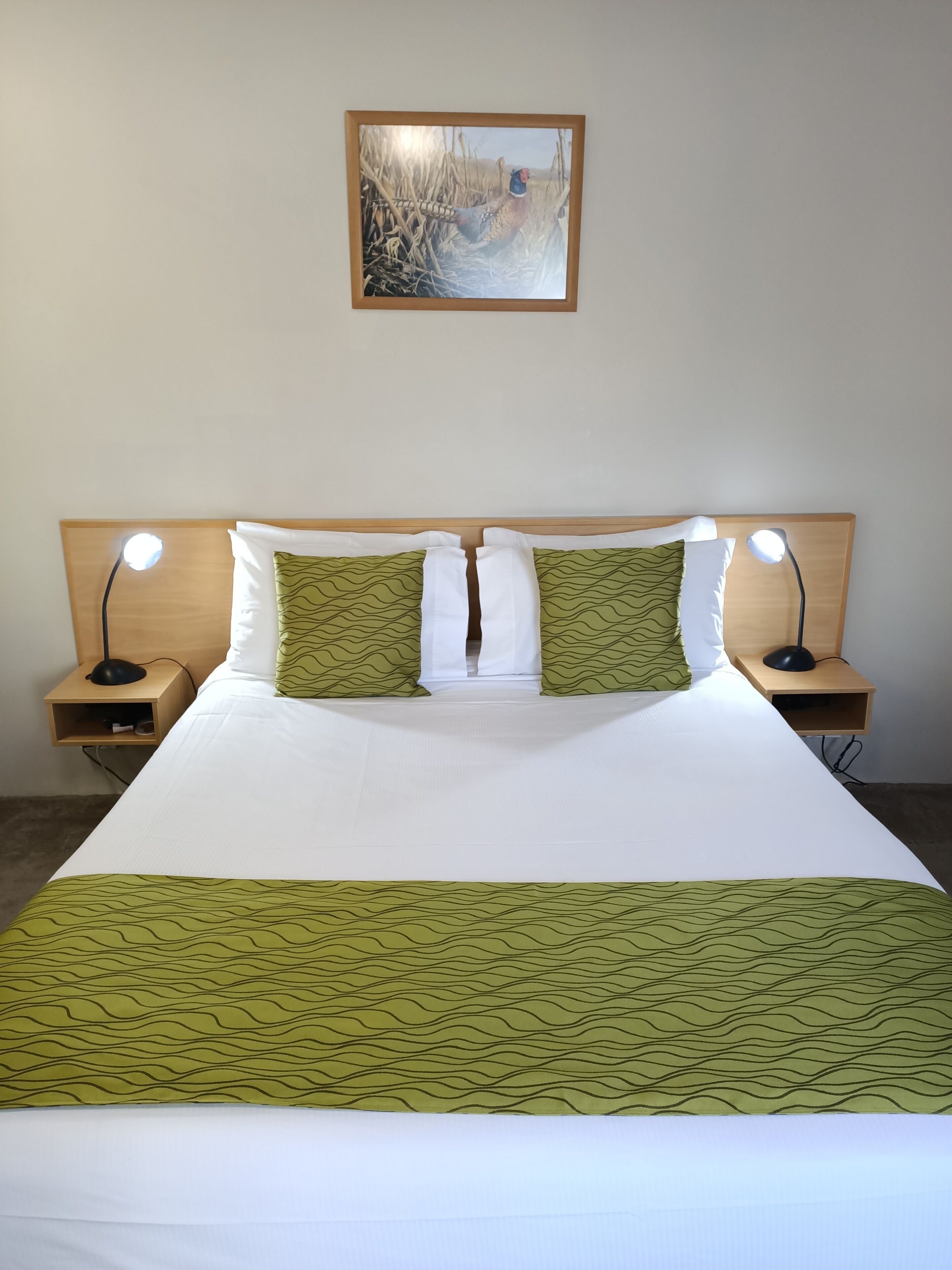 A neatly made bed with white and green bedding, two bedside lamps, and a framed picture on the wall.