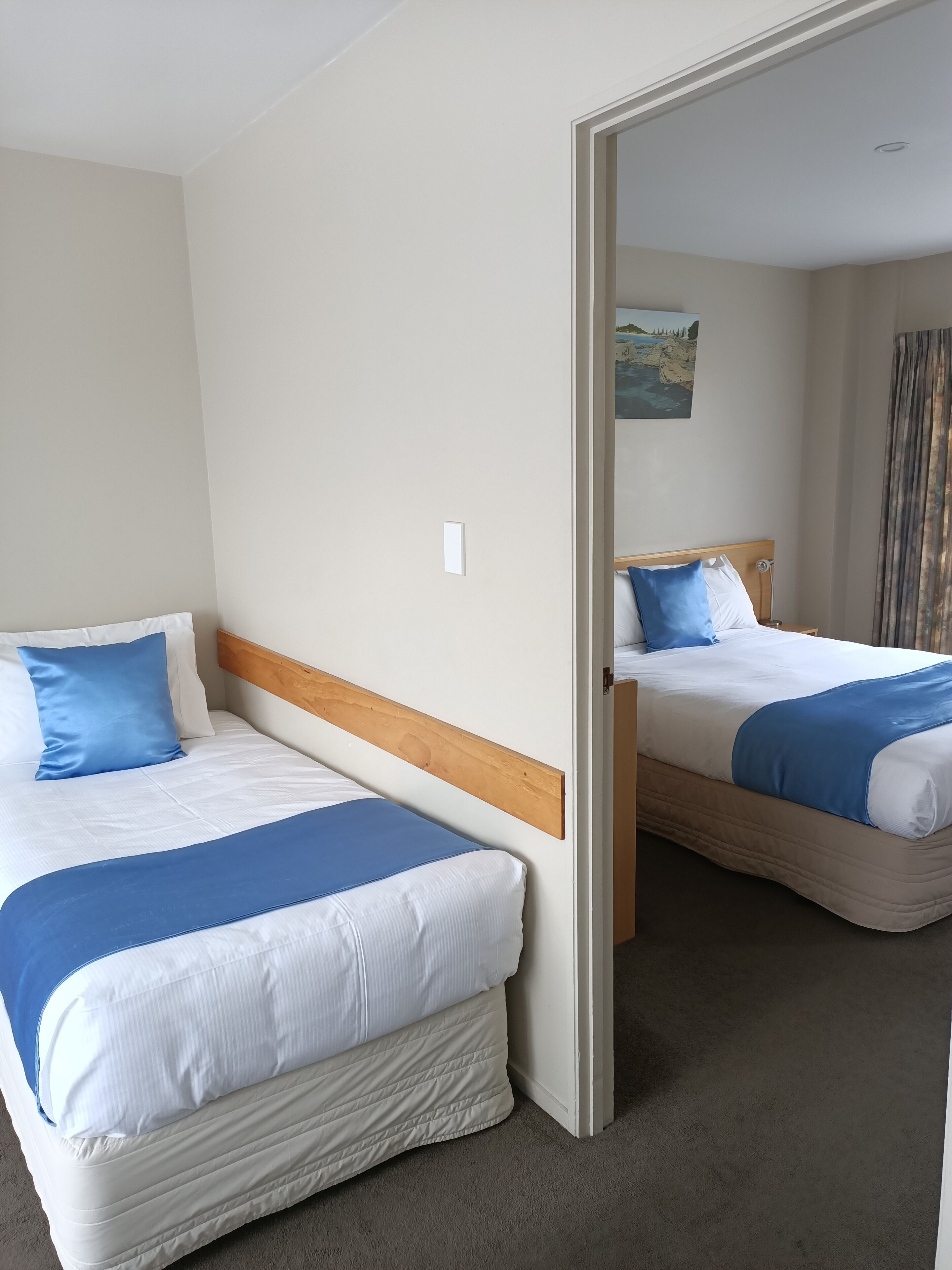 A hotel room with two beds, each with a wooden headboard, white bedding, and blue accents.