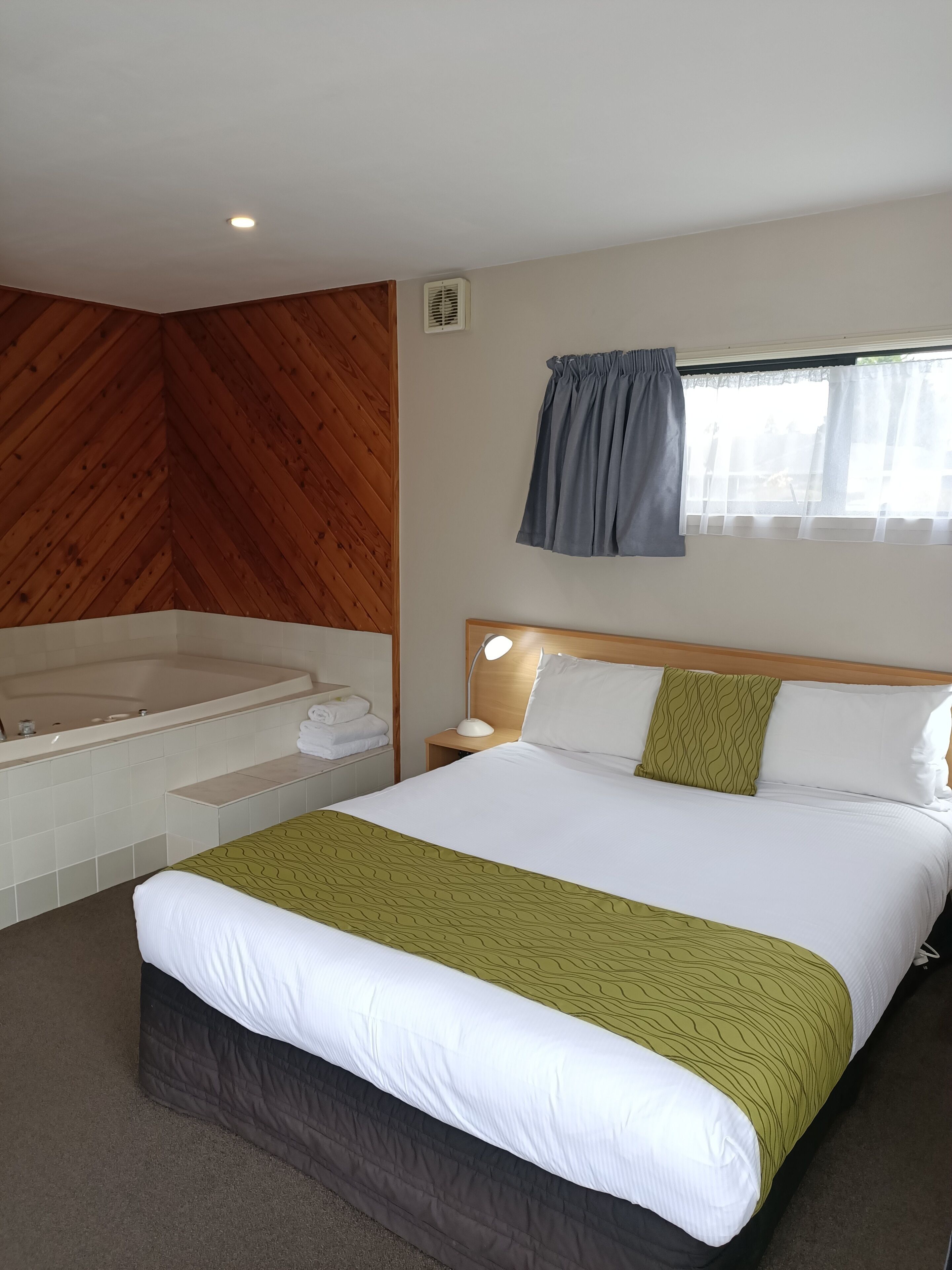 Habitación de hotel con una cama grande, una bañera independiente, una ventana con cortinas y una pared de madera.