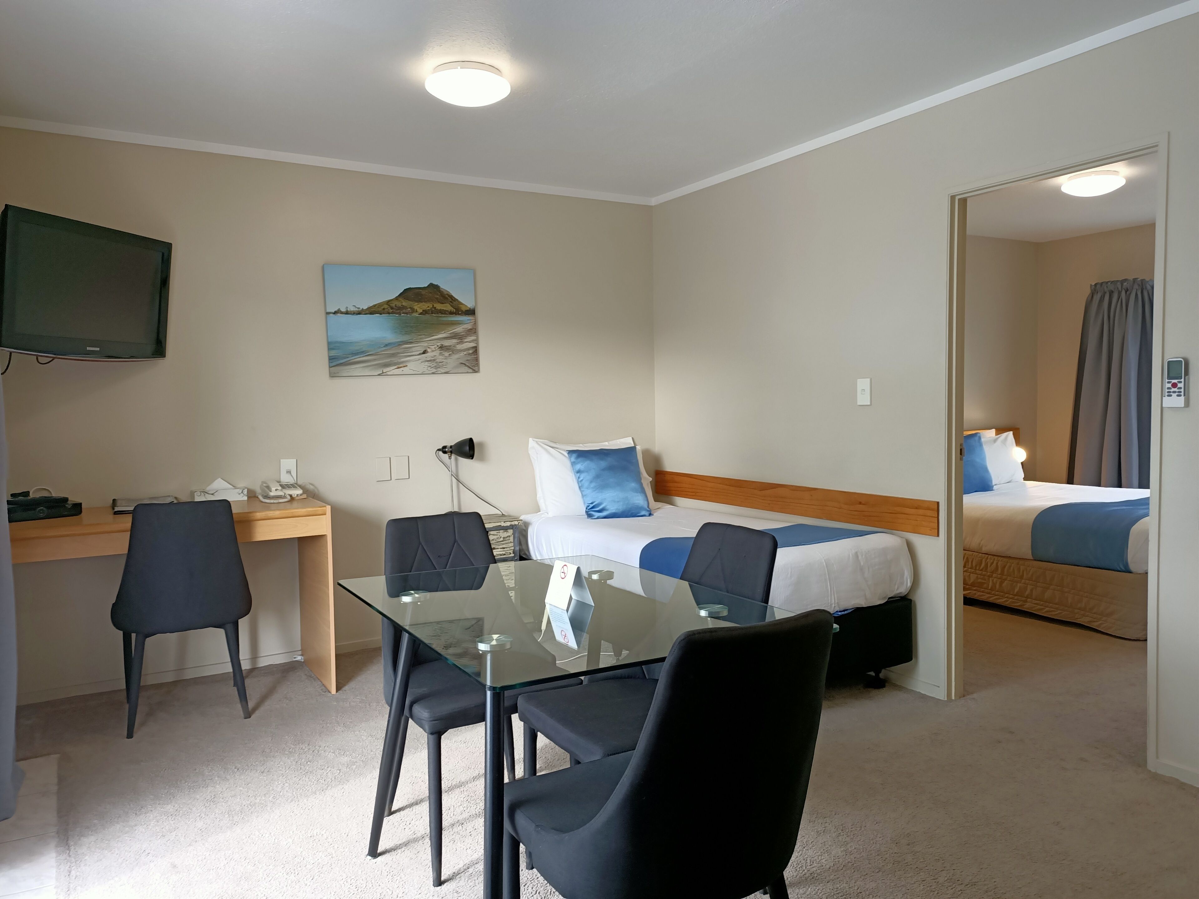 Une chambre d’hôtel équipée d’un bureau, de deux chaises, d’un lit, d’une télévision et d’un tableau au mur.