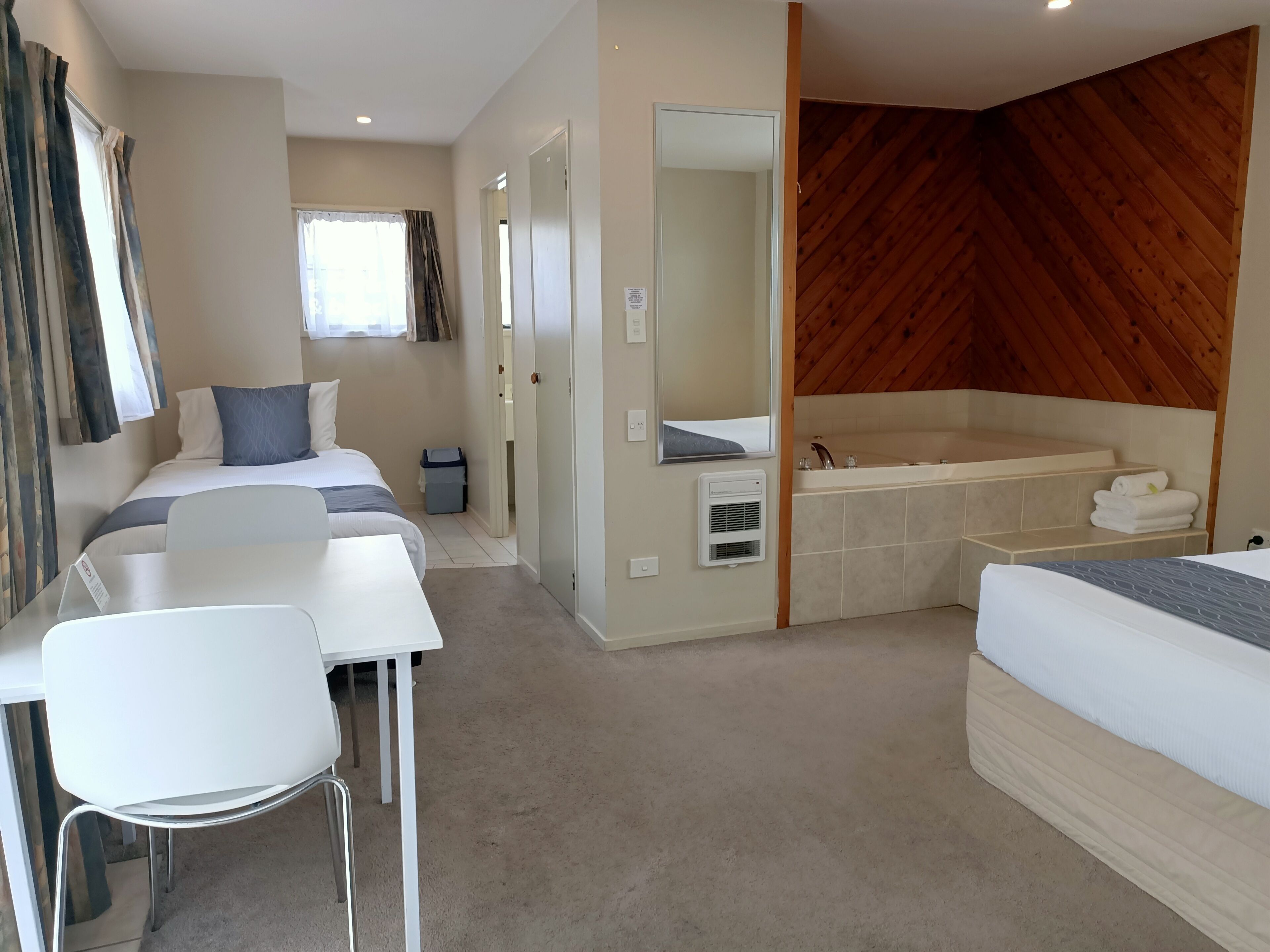 Une chambre d’hôtel moderne comprenant un lit, un bureau, une chaise, une salle de bain avec baignoire et un mur en bois.