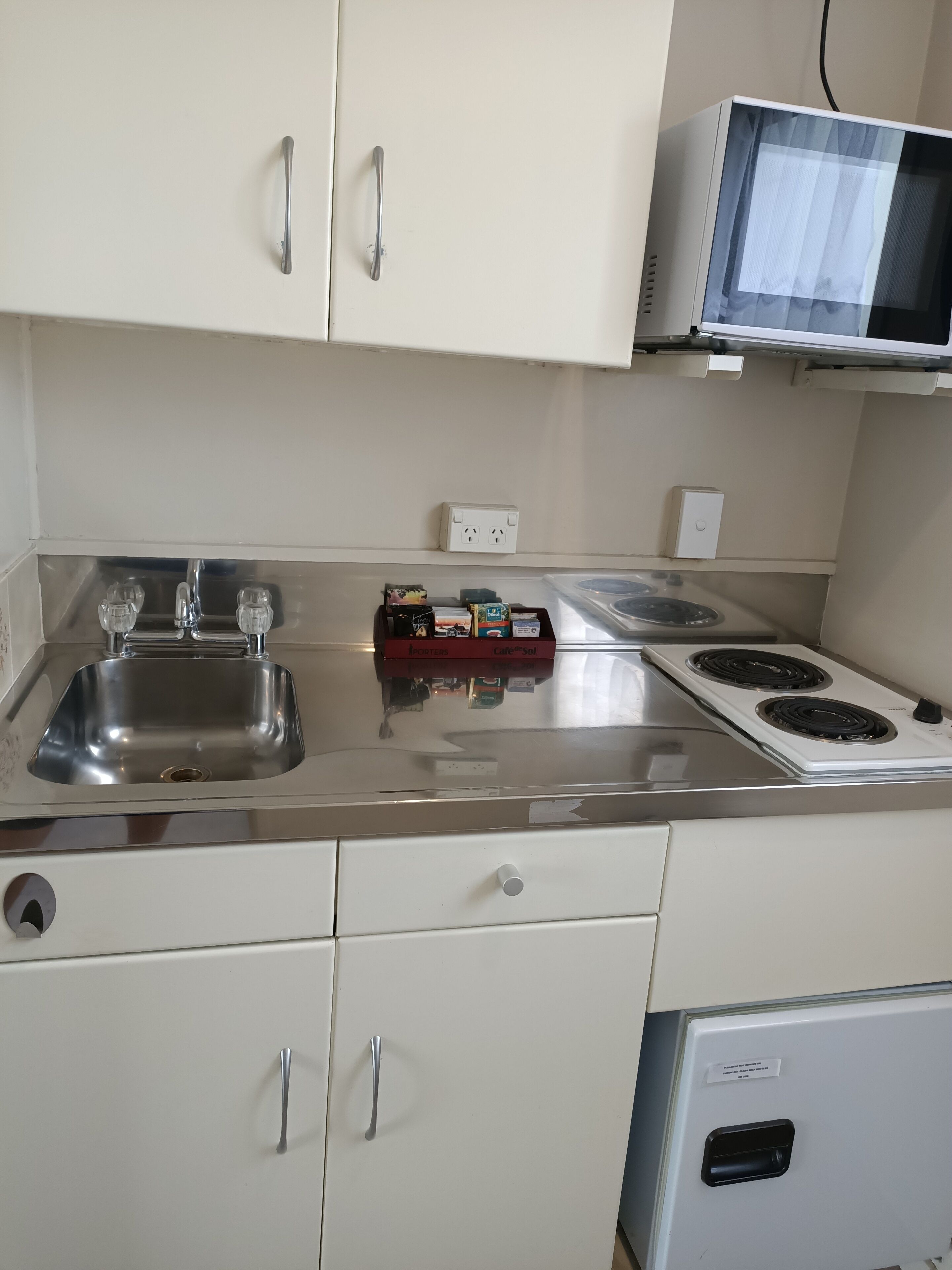 A kitchen with a stainless steel sink, two ovens, a microwave, and white cabinets.