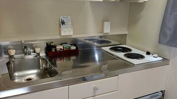 A compact kitchen with a stainless steel sink, a microwave, and a stove. There are cabinets with silver handles and a small refrigerator below the counter.