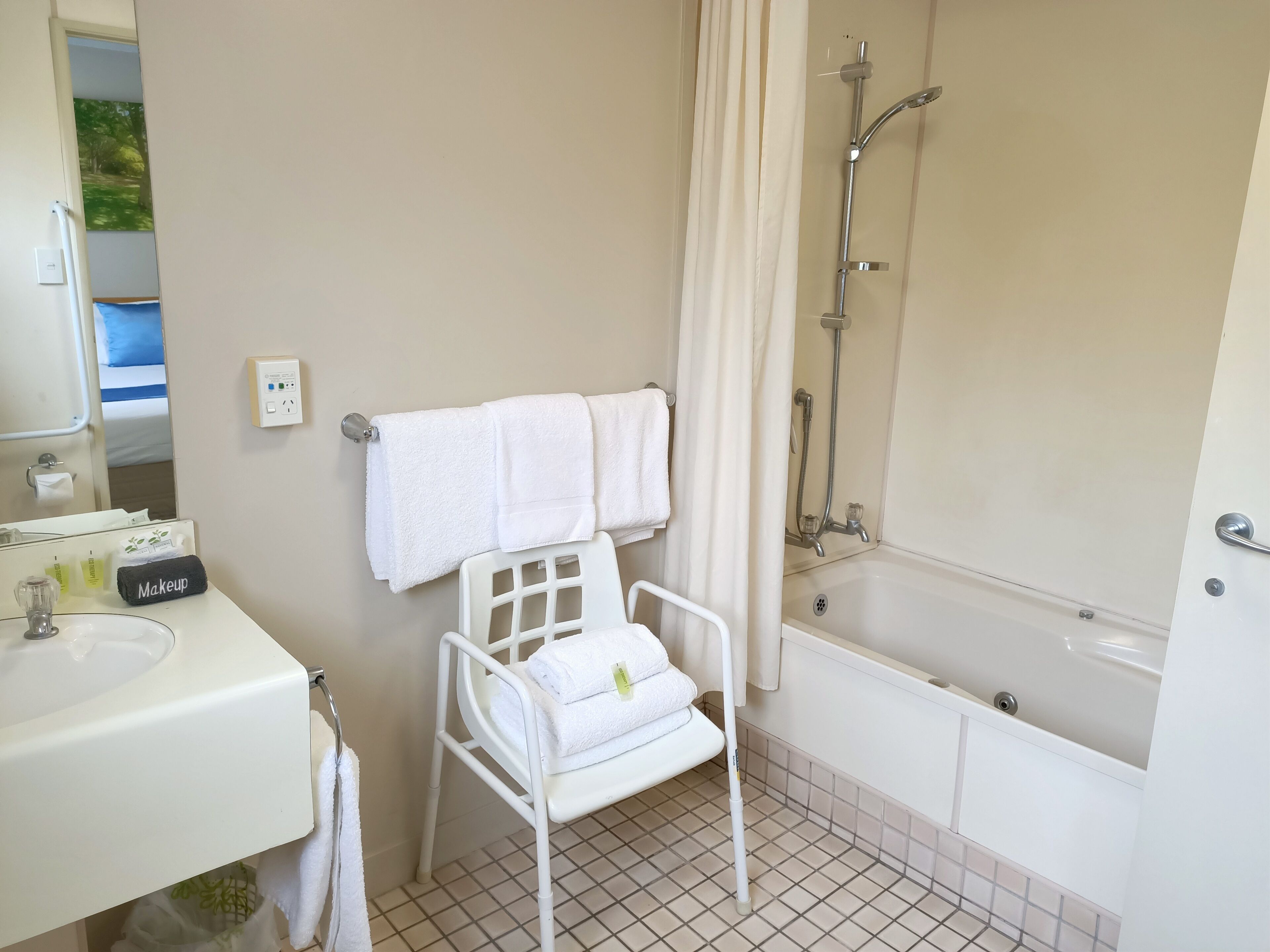 Een badkamer met een witte wastafel, een witte stoel met handdoeken, een bad en een douche.
