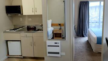 Habitación de hotel compacta con kitchenette, cama, baño pequeño y vistas al exterior.