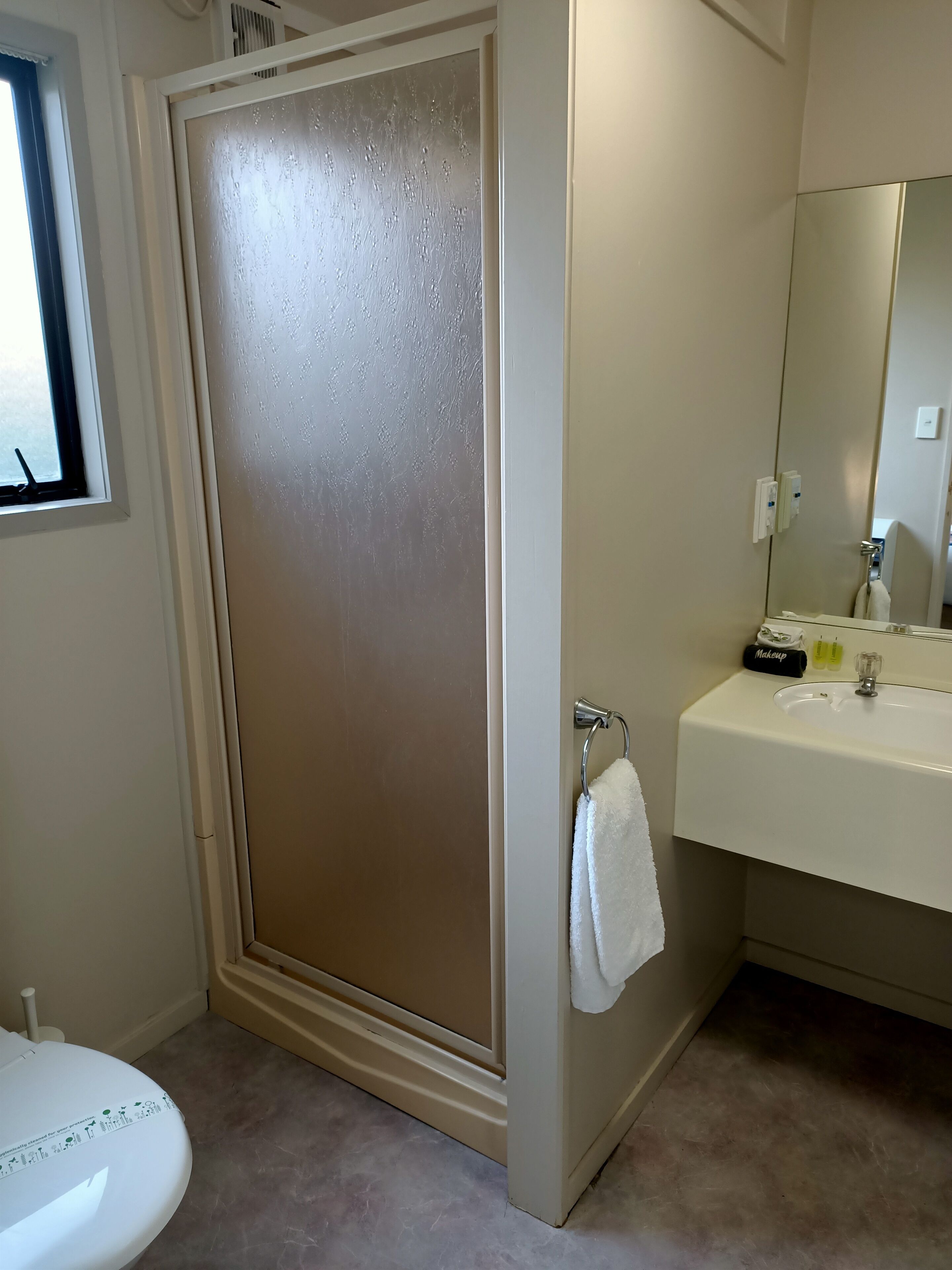 A bathroom with a frosted glass shower door, a white sink with a mirror, and a white towel hanging on a rack.