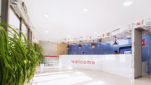 A reception desk with a 'welcome' sign, a blue wall with decorative elements, and a glass door entrance.